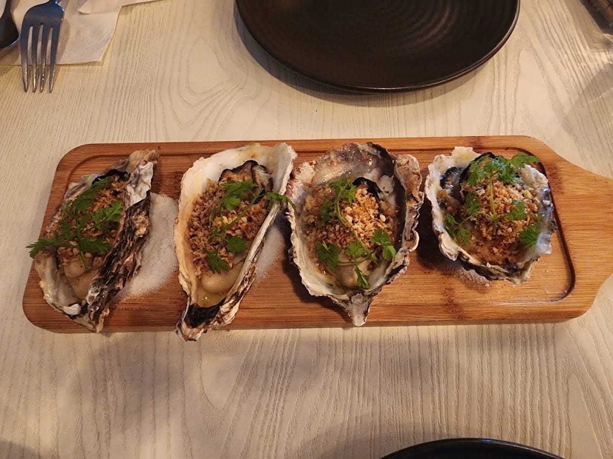 Four Italian-style baked oysters with gremolata crumbs on a wooden board